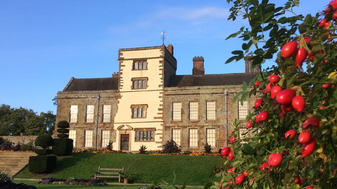 An autumn view of Canons Ashby with rosehip bushes in foreground